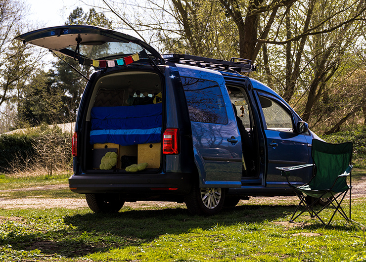 Ein umgebauter Van mit offenem Kofferraum steht auf einem Campingplatz.